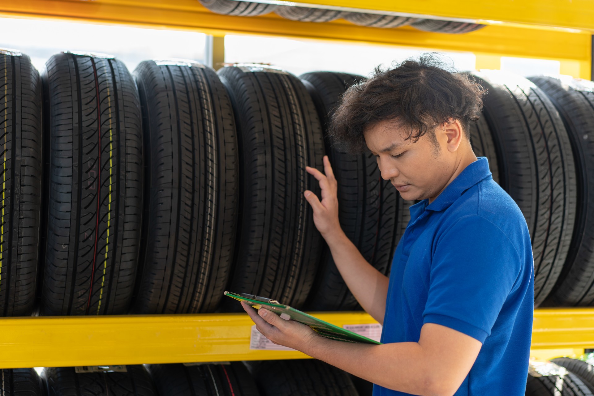 Un technicien asiatique vérifie les nouveaux pneus roue sur une étagère à l’atelier du magasin d’automobiles et au service de réparation automobile