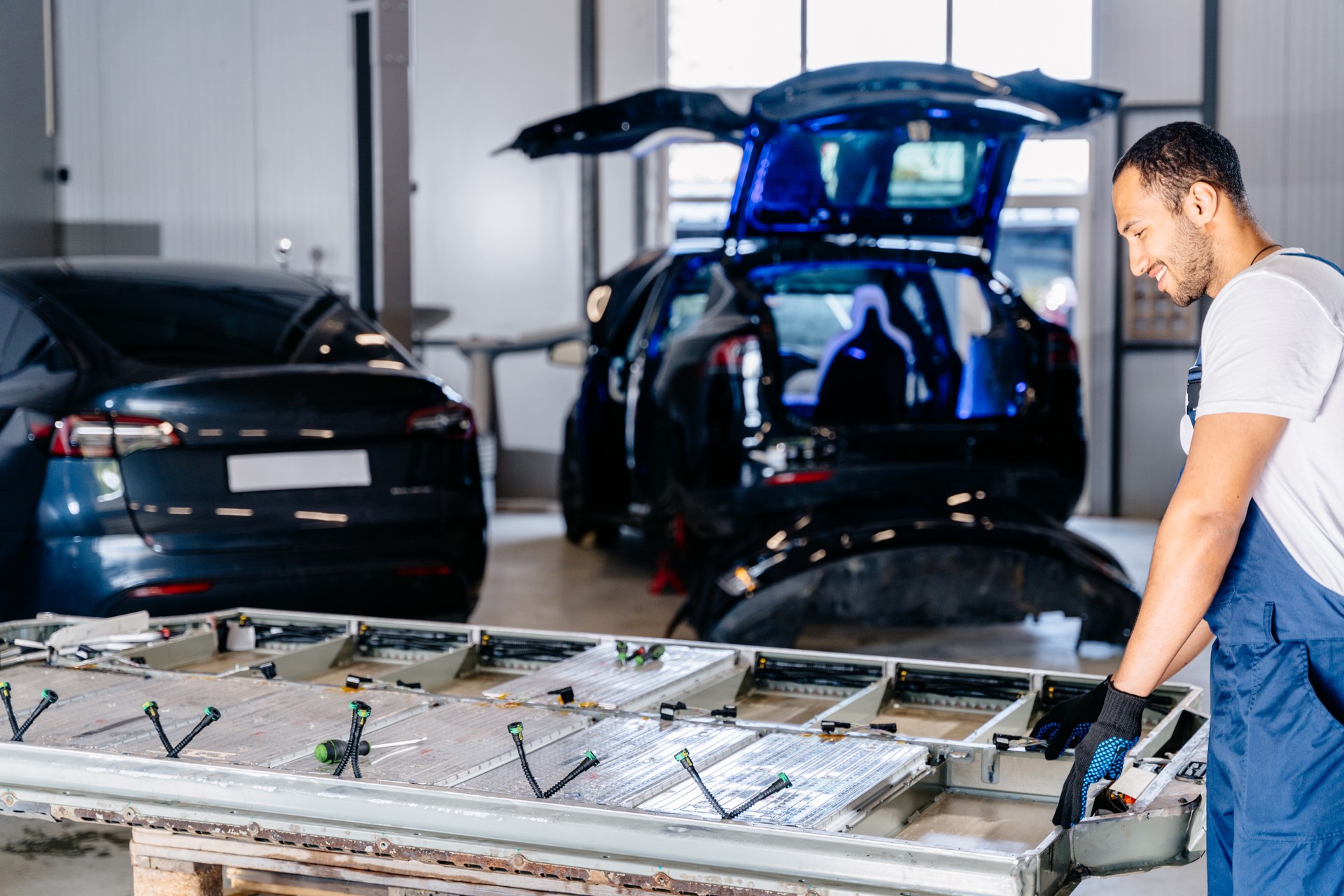 Un technicien masculin arabe souriant positif s’engage avec un module de cellule de batterie de voiture EV dans un service automobile. Entretien de la réparation de la batterie de la voiture.